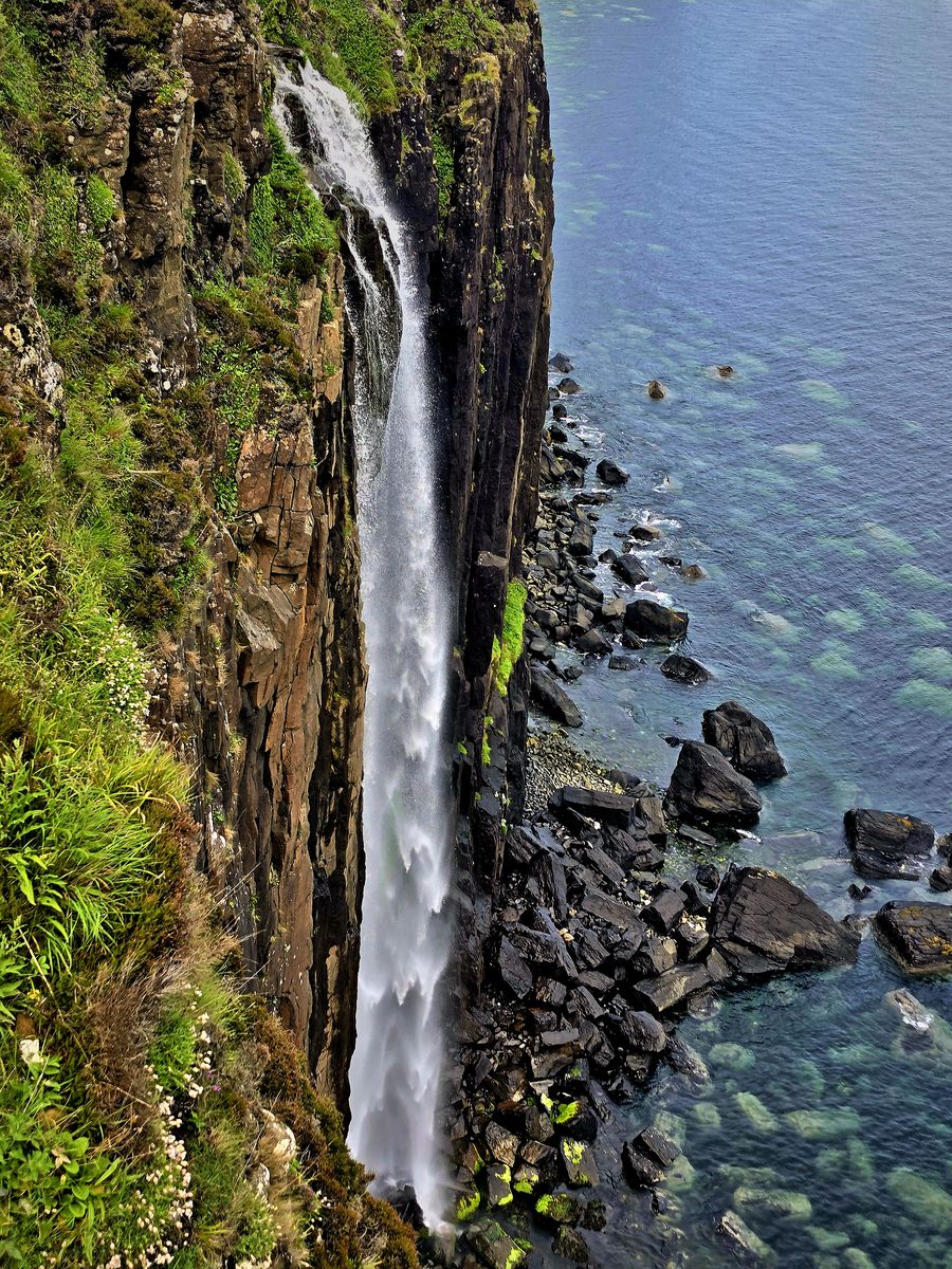 Waterfall plunging off a sea cliff into clear blue water